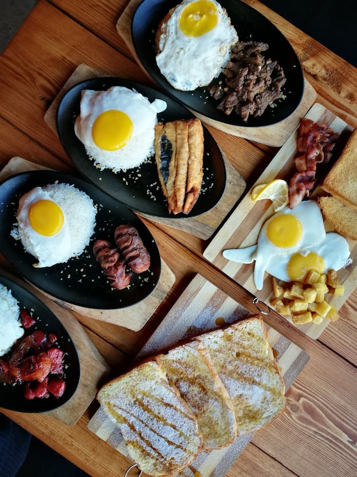 An appetizing breakfast spread featuring eggs, meats, toast, and rice on a wooden table.